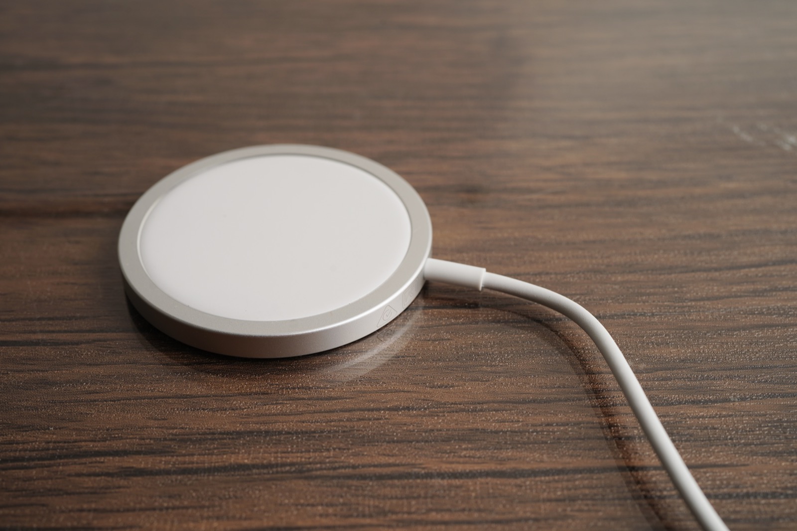 A round magnetic MagSafe-style wireless charging pad with cable on a wooden desk