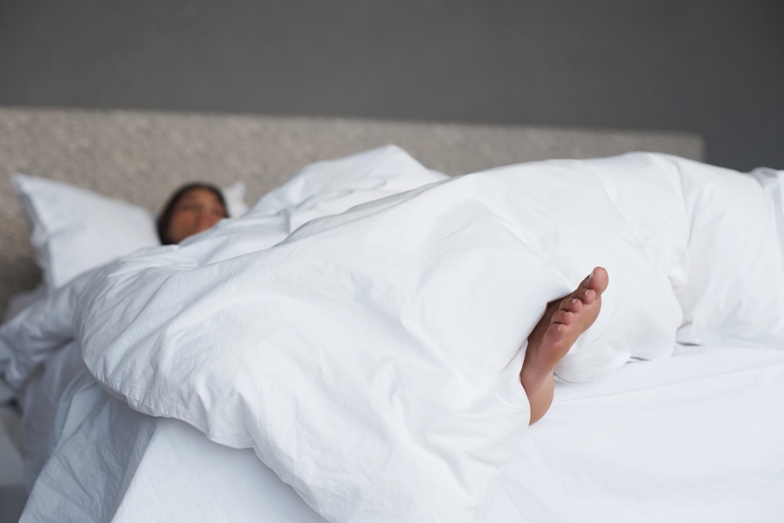 A sleeper resting under a lightweight white cooling comforter