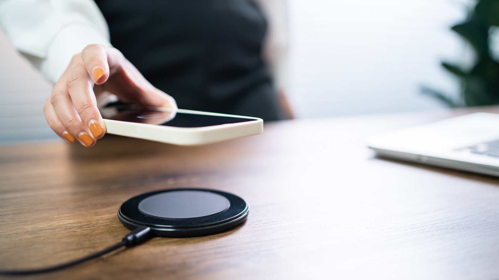 A smartphone being placed onto a round wireless charging pad on a desk
