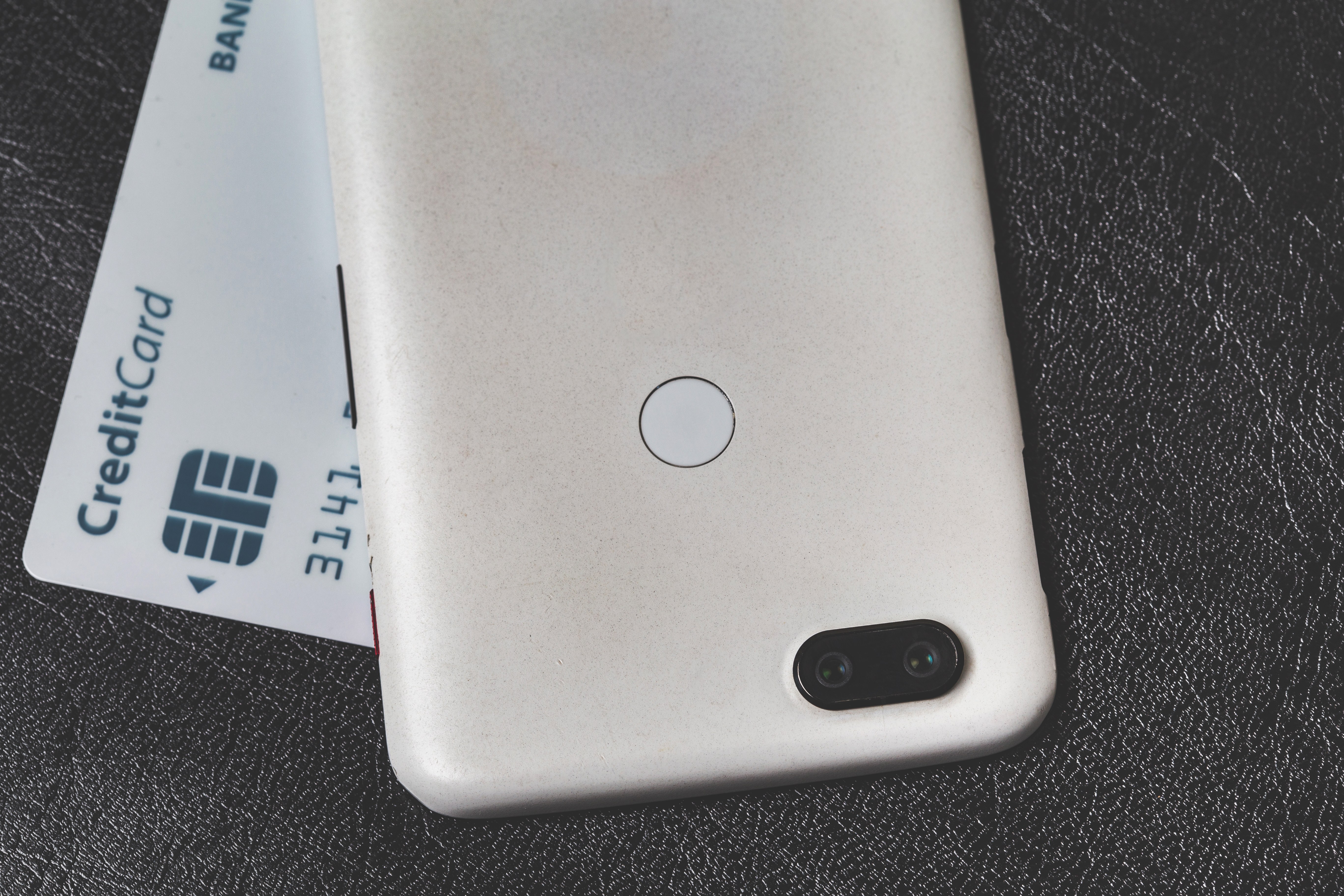 A smartphone resting on a leather surface next to a credit card, illustrating a magnetic card wallet accessory