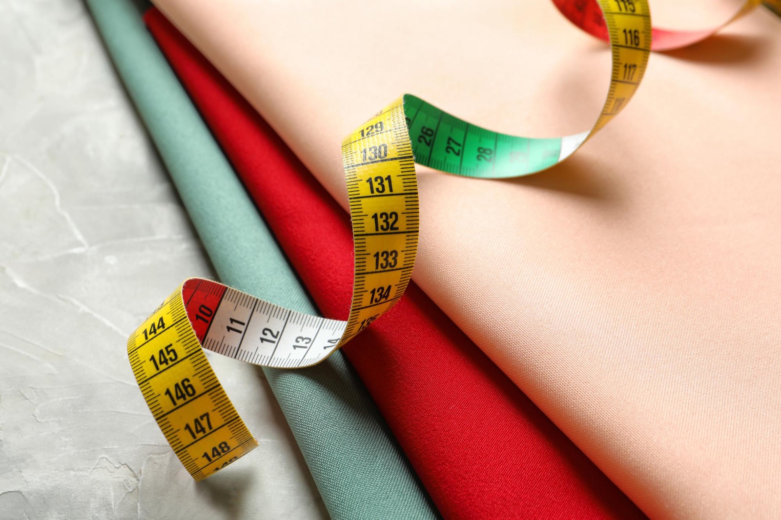 A soft tailor measuring tape draped over folded summer dress fabrics