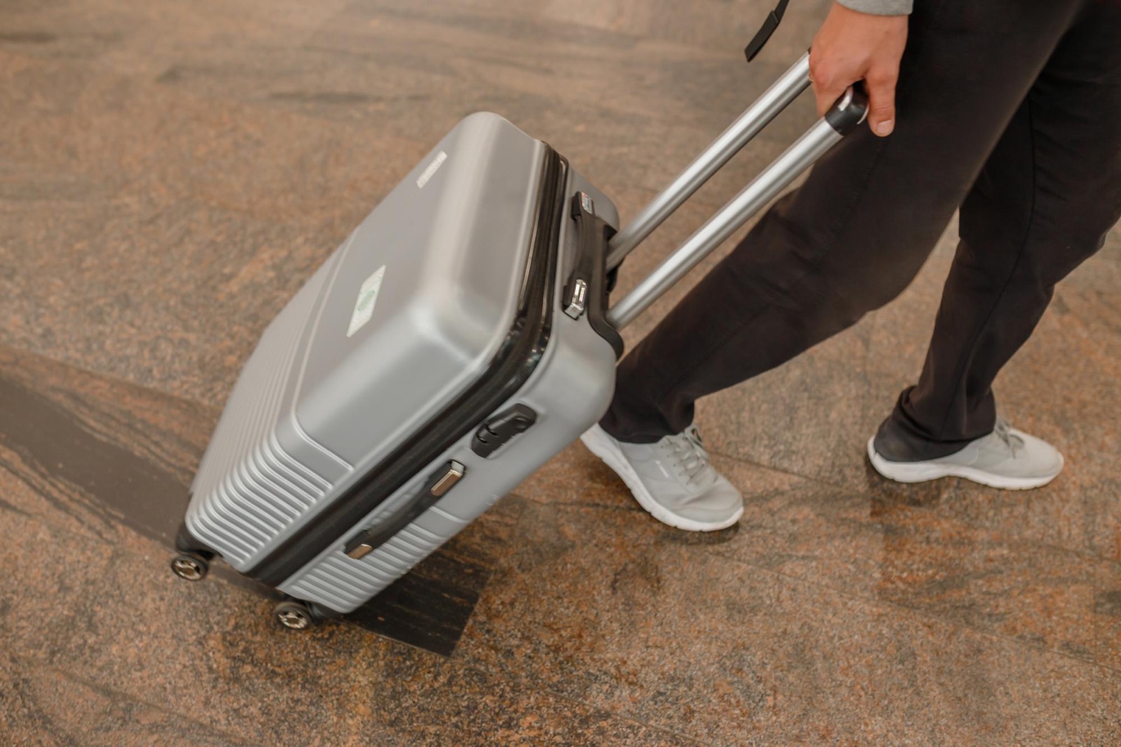 A traveler pulling a grey hardside spinner suitcase across a terminal floor