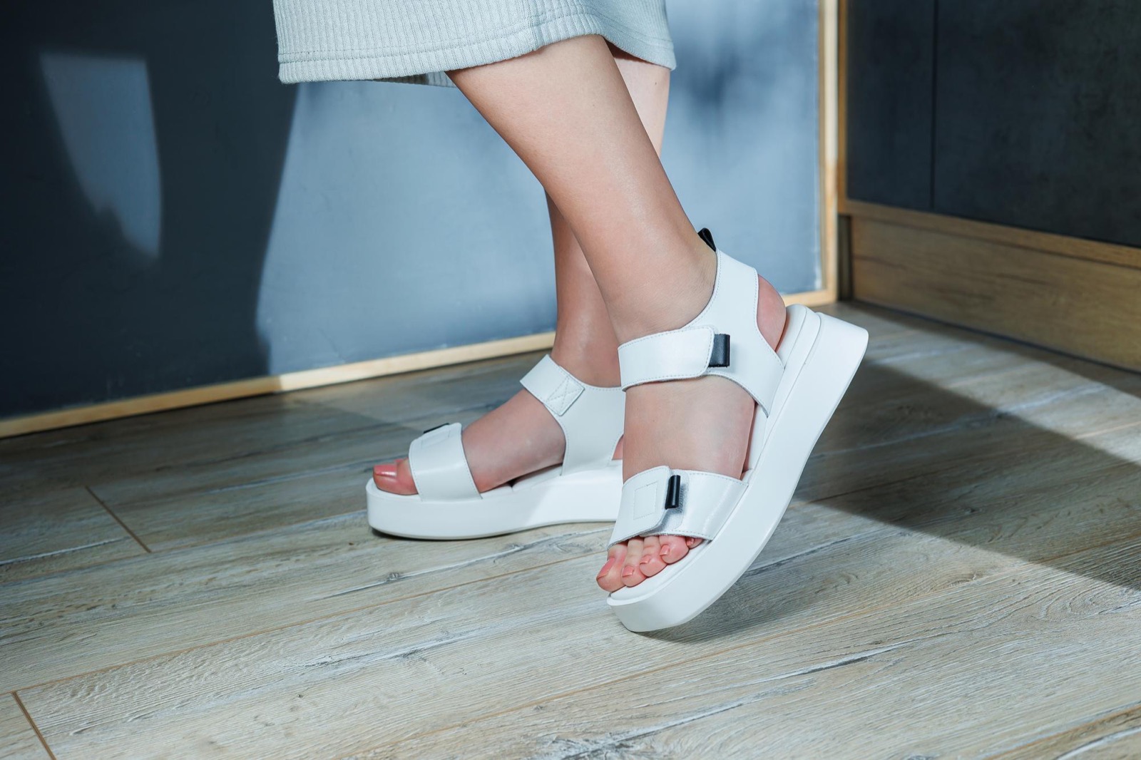 A woman wearing white adjustable-strap summer sandals, shown from the side