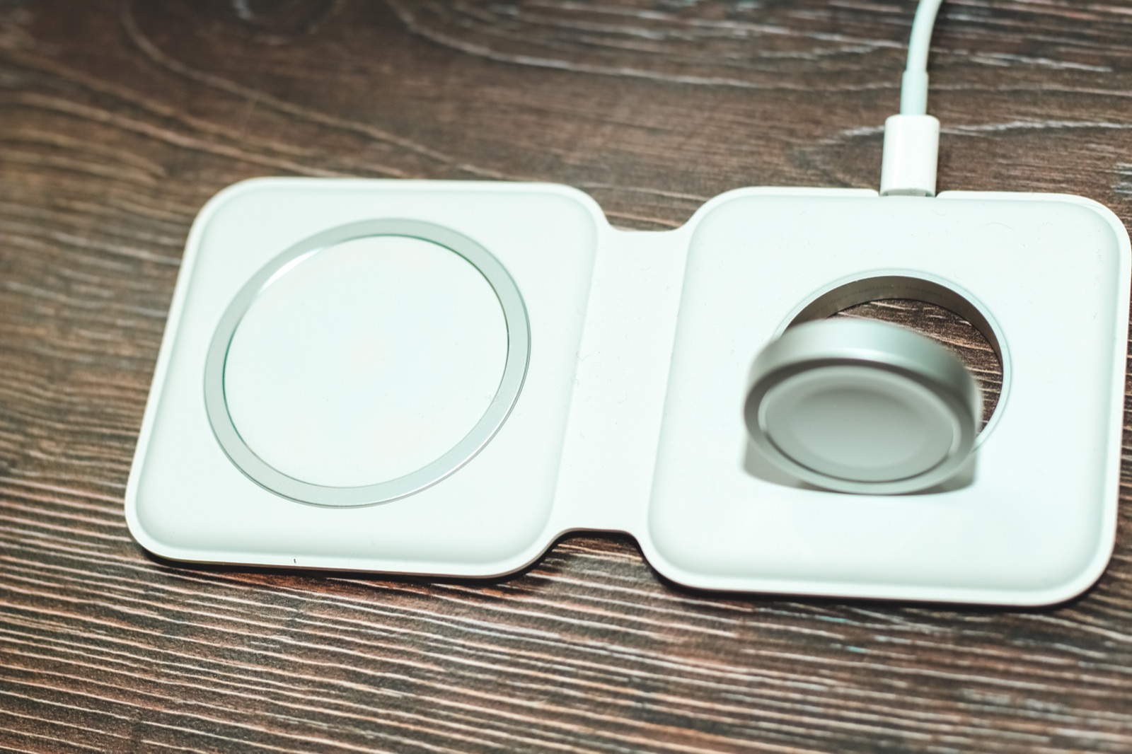 Apple Watch charging puck and a wireless charging pad on a wooden desk