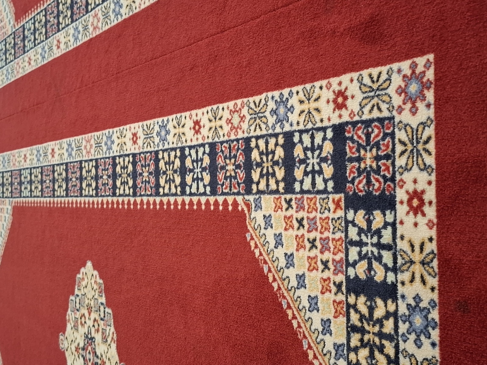 Close-up of a hand-knotted wool Kazak oriental rug with intricate geometric border motifs in red, navy and cream