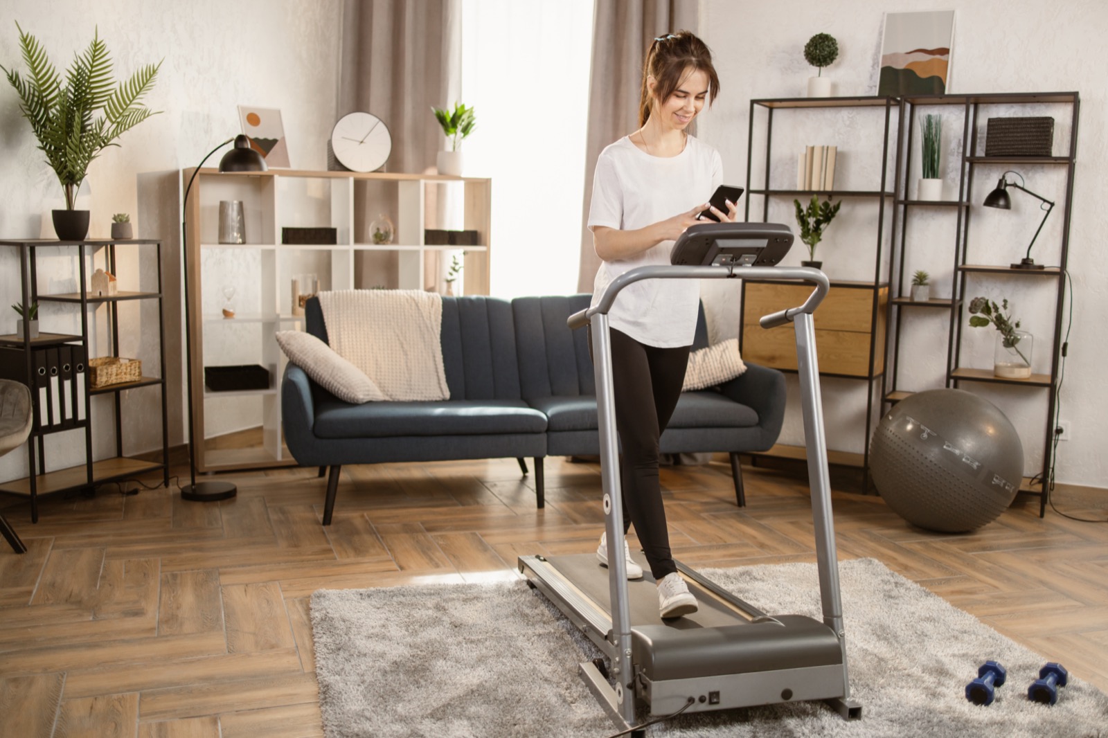 Compact folding treadmill set up in a living room while a person checks their phone