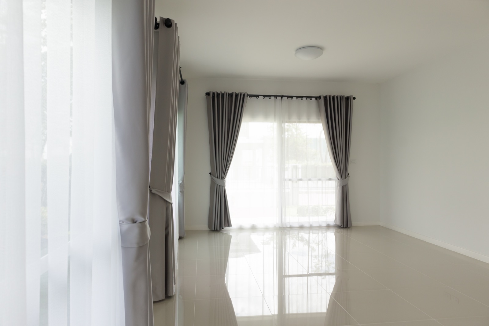 Floor-to-ceiling neutral curtains mounted near the ceiling and falling to the floor in a bright living room