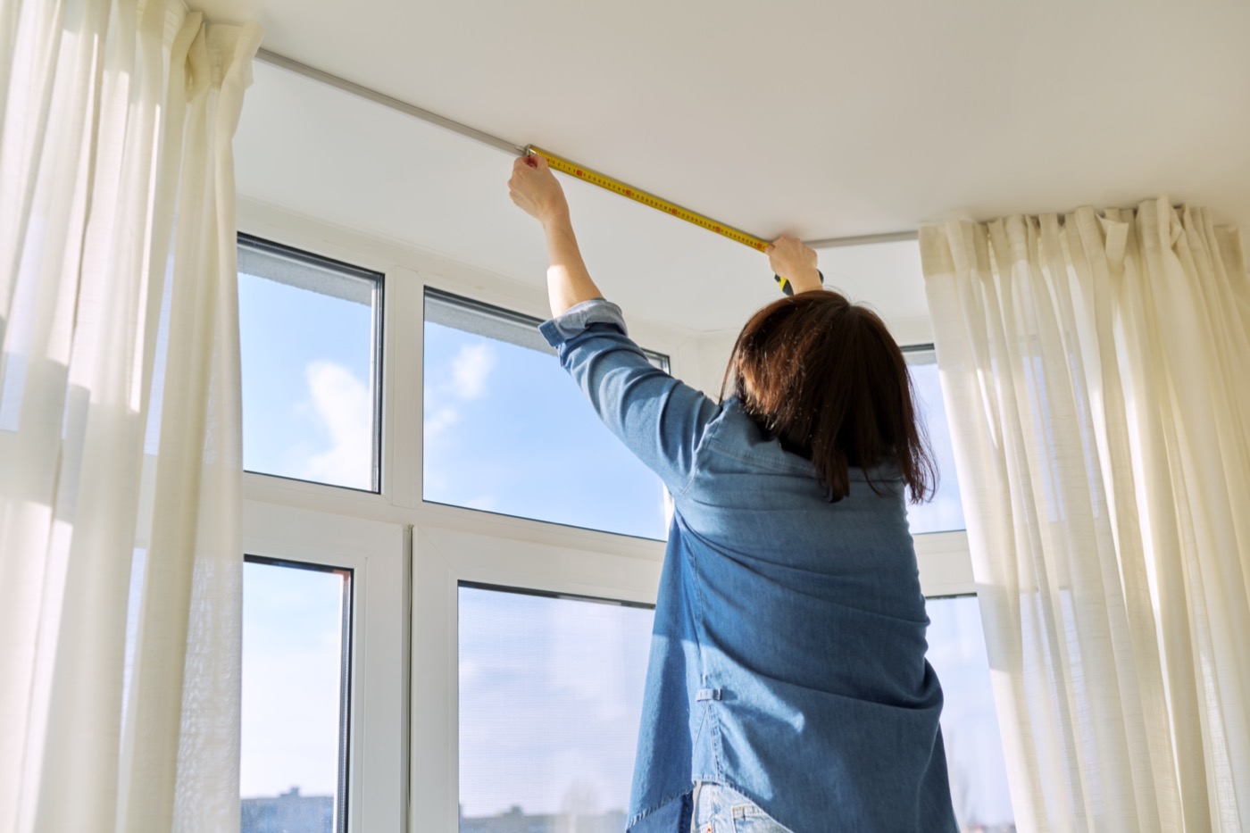 Measuring the curtain rod width above a living room window with a tape measure