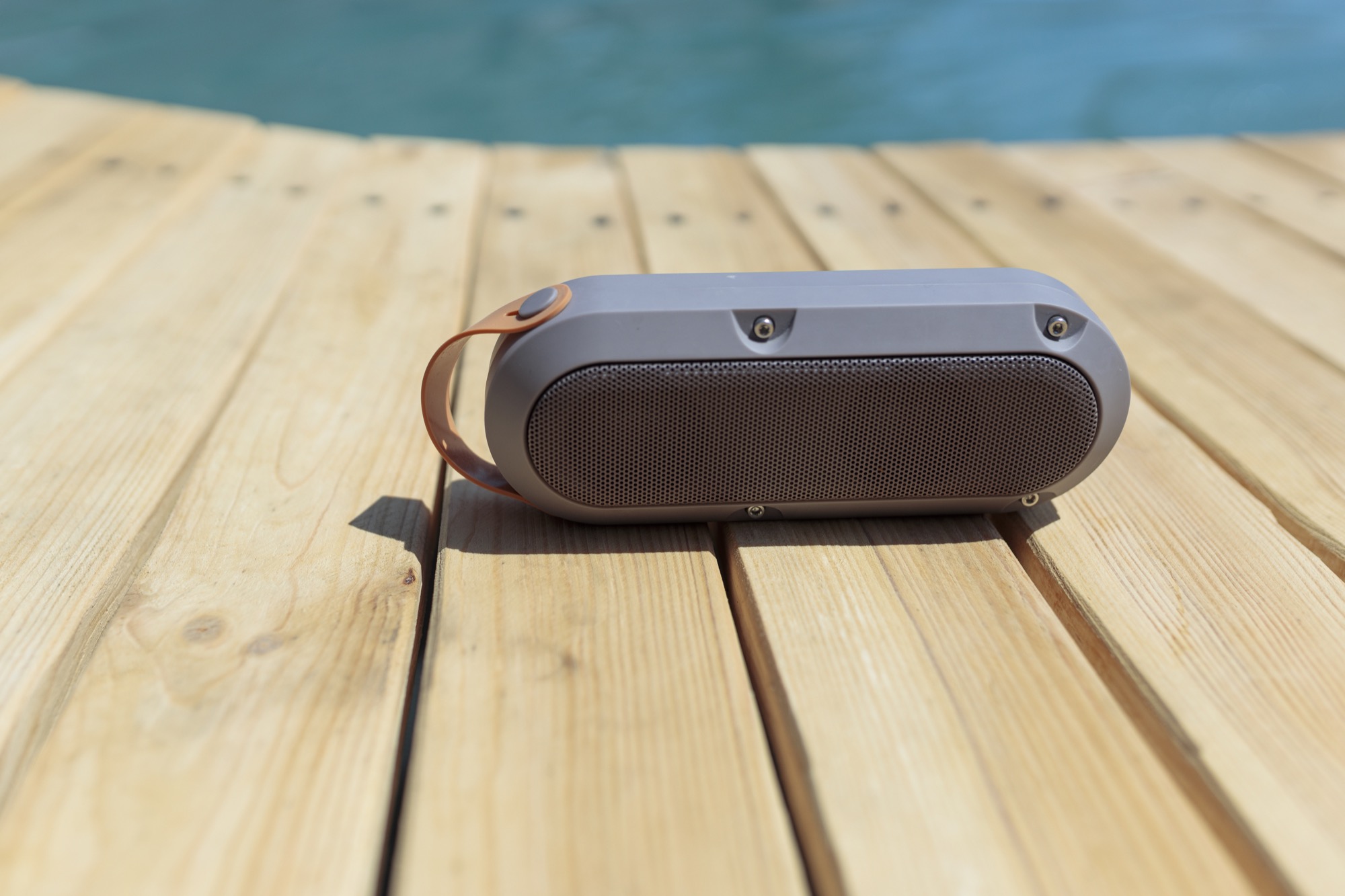 Portable Bluetooth speaker on a wooden deck beside a swimming pool