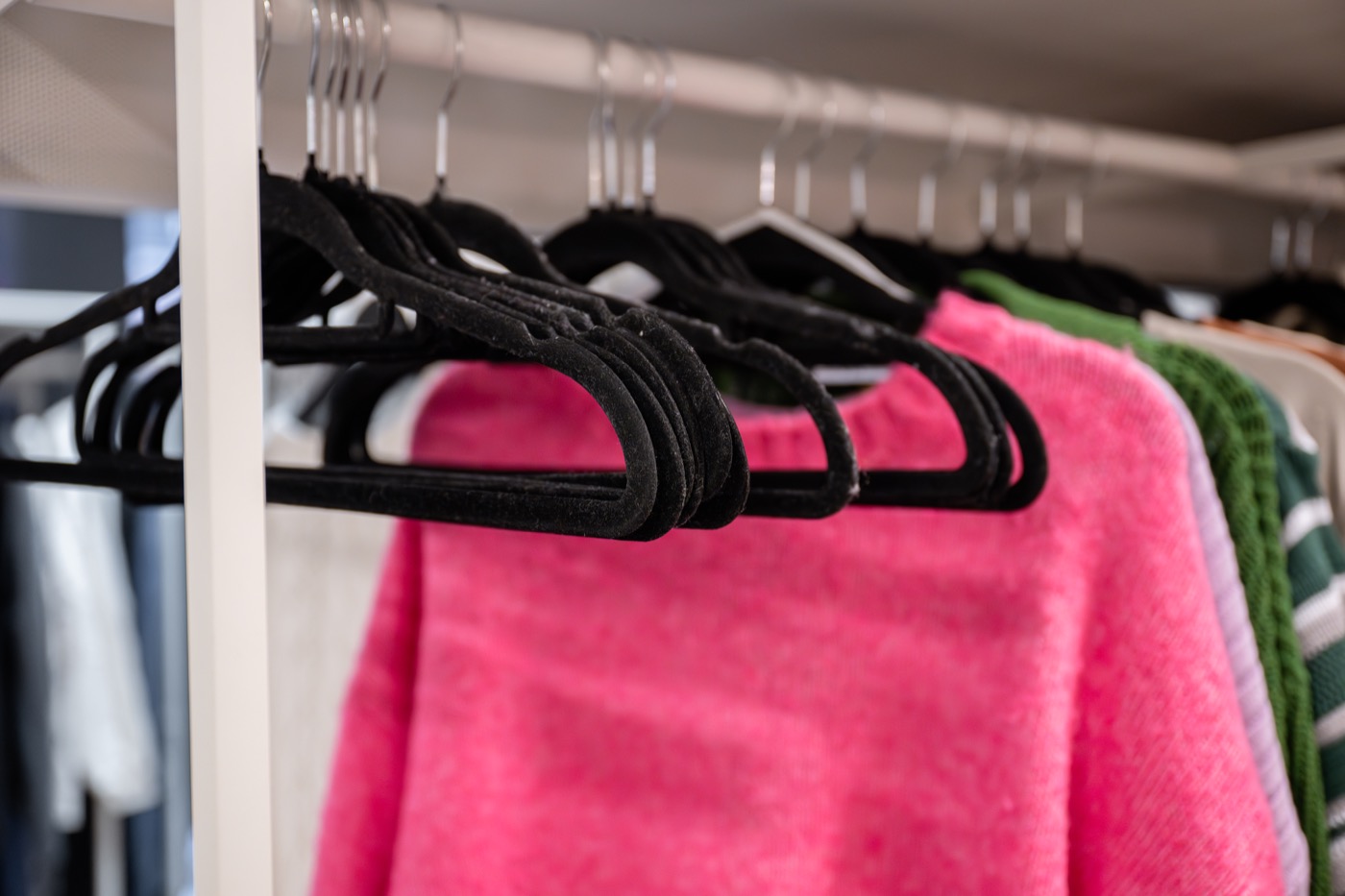 Row of black velvet non-slip hangers holding sweaters on a closet rail