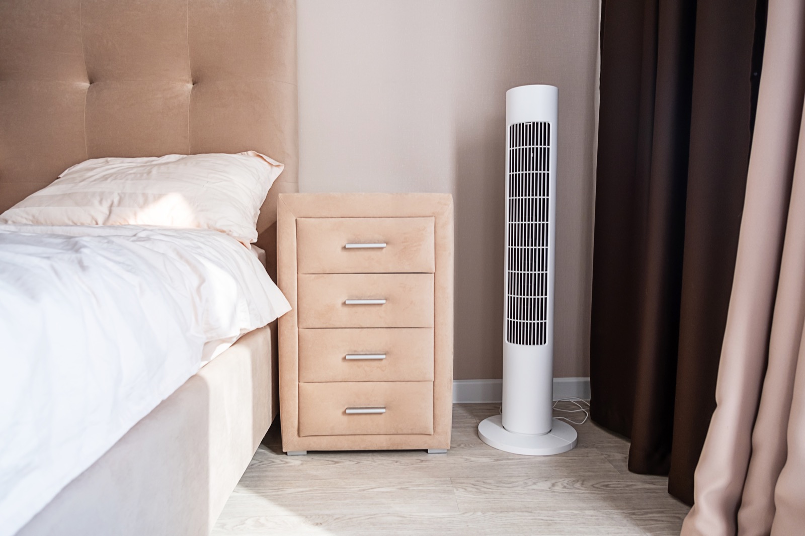 White bladeless-style tower fan beside a bed in a calm bedroom